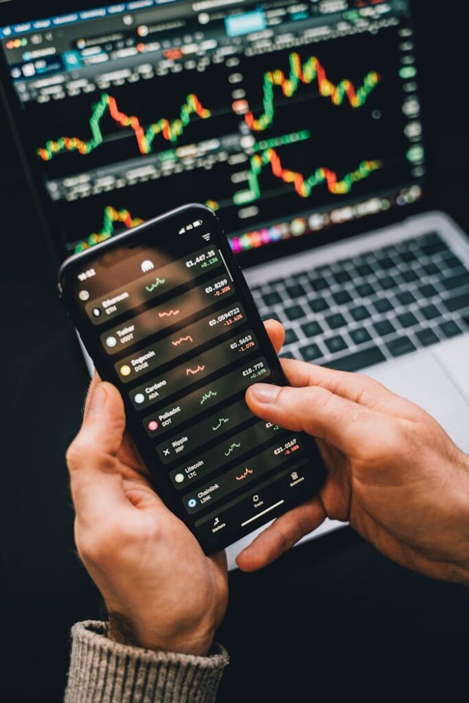 pexels-photo-6771900 Hands holding smartphone with stock app, laptop displaying charts. Perfect for financial and technology themes.